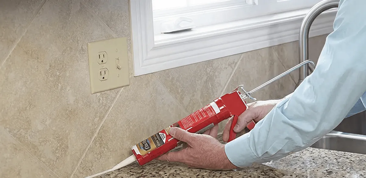 Handyman applying caulk along a kitchen backsplash and countertop seam in Mobile, AL